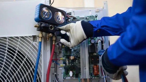 Technician connecting refrigerant gauges to an air-conditioning unit for regassing